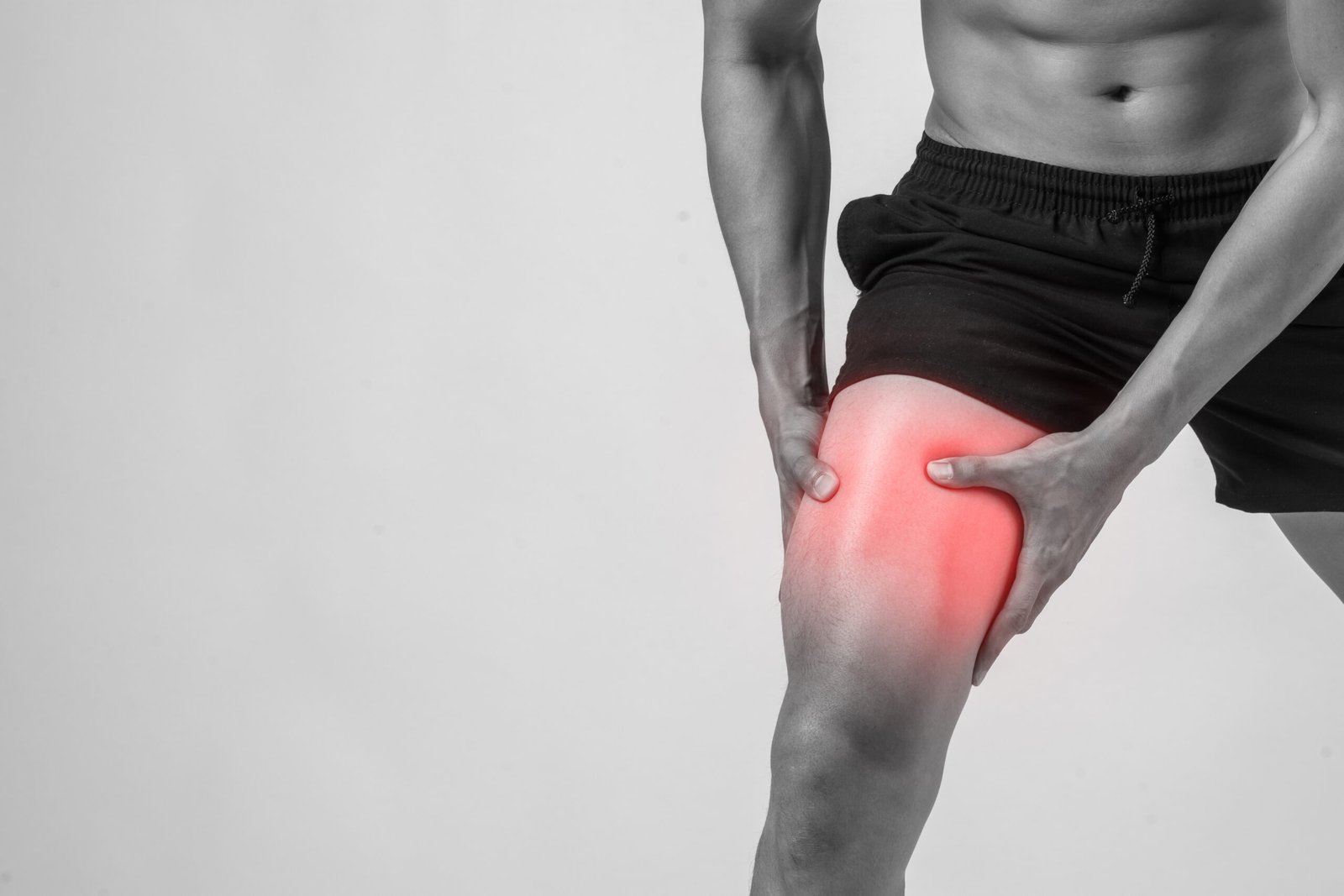 Young sport man with strong athletic legs holding knee with his hands in pain after suffering ligament injury isolated on white.